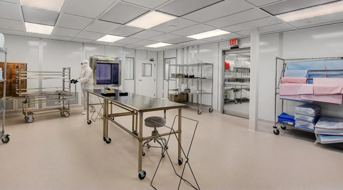 A sterile room with a person in gowning, medical supplies on shelving, and various equipment on mobile tables.