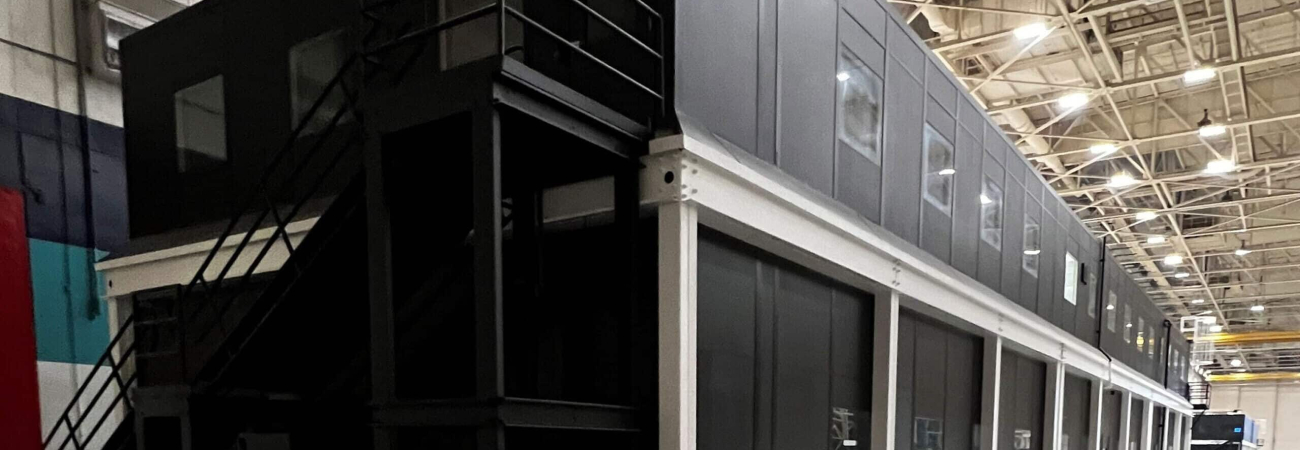 A black, two-story modular office building in a warehouse.