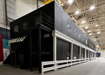 A black, two-story modular office building in a warehouse.