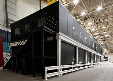 A black, two-story modular office building in a warehouse.