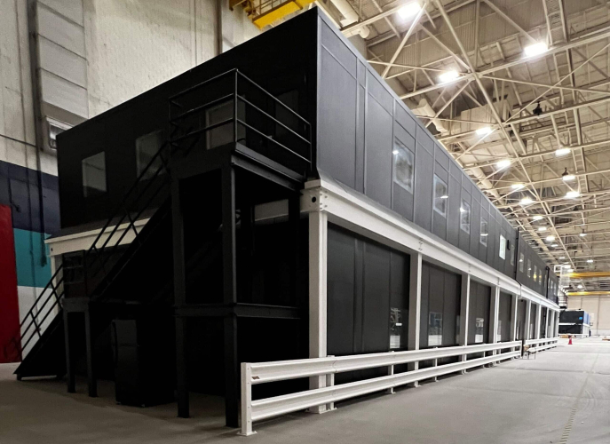 A black, two-story modular office building in a warehouse.