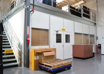 Modular mezzanine structure with storage boxes and equipment on the ground level in an industrial facility.
