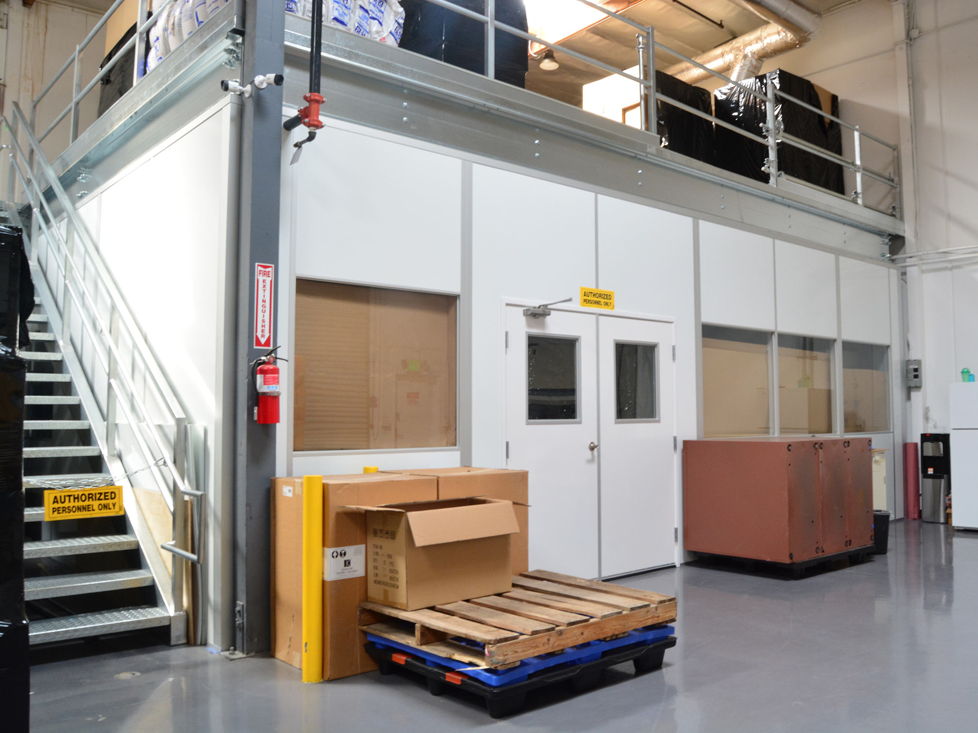 Modular mezzanine structure with storage boxes and equipment on the ground level in an industrial facility.
