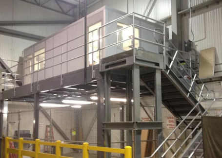 A modular mezzanine office space elevated above a workshop area with metal stairs and railings.