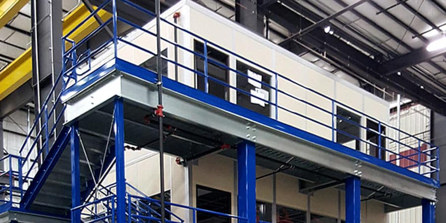 A blue steel mezzanine structure with railings and stairs inside a warehouse.