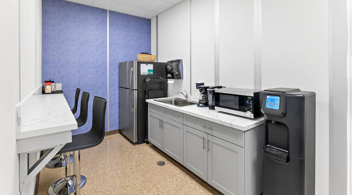 Compact lunch room in a modular office with a refrigerator, microwave, sink, coffee maker, and water dispenser.