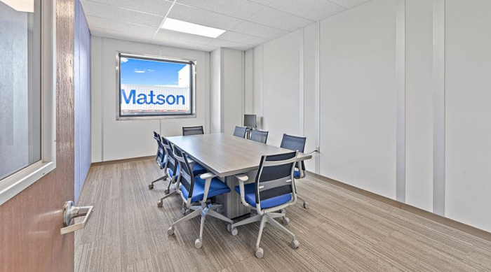 A modular conference room with a central table and chairs, featuring a window with the "Matson" logo visible outside.