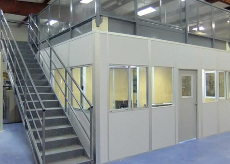 A mezzanine structure with a staircase leading to an upper level above an enclosed office space in a warehouse. The mezzanine is supported by metal beams and includes safety railings around the perimeter.