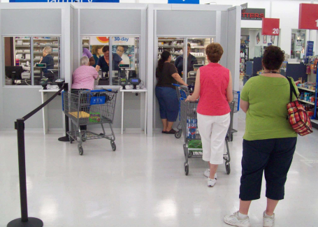 Modular pharmacy checkout counters with customers waiting in line, featuring prefabricated enclosures by Allied Modular.