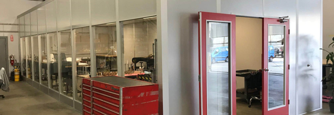 A modular office with glass windows and red doors installed inside a warehouse space.