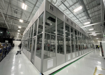 A modular factory structure with glass walls and a metal frame, located inside a large, well-lit industrial facility.