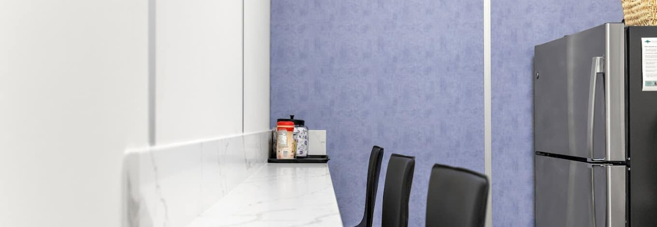 Inside a modular warehouse break room, with chairs, a refrigerator, and blue and white panels.