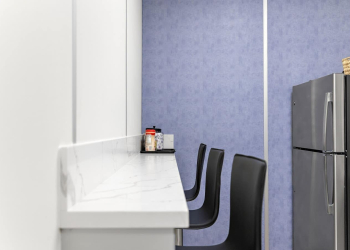 Inside a modular warehouse break room, with chairs, a refrigerator, and blue and white panels.