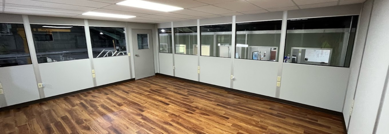 A spacious and well-lit interior of a modular building featuring wood flooring and large windows.