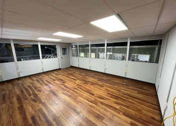 A spacious and well-lit interior of a modular building featuring wood flooring and large windows.