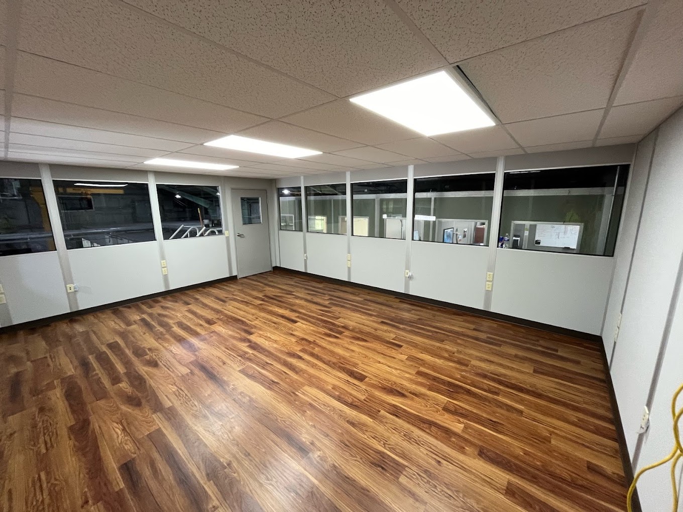 A spacious and well-lit interior of a modular building featuring wood flooring and large windows.