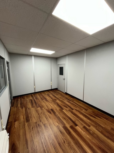 A modular office building with large windows and a door, assembled inside a warehouse.