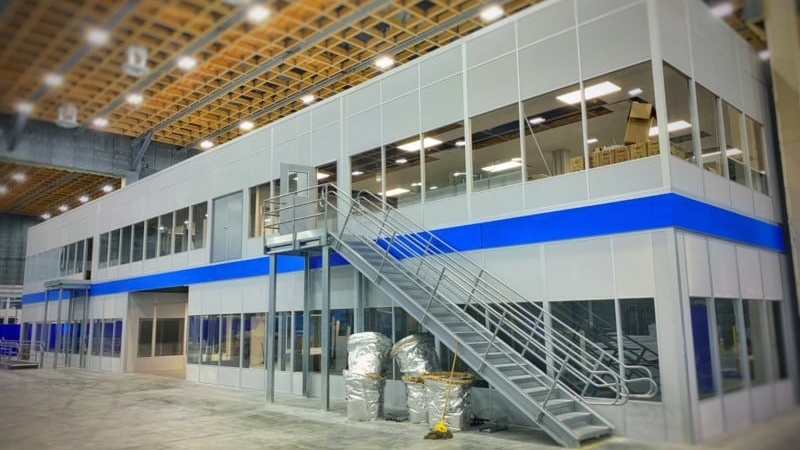 A modern, industrial-style office space with an external staircase leading to a second-floor area inside a large warehouse.