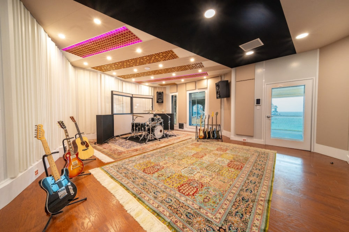 A modular sound studio featuring musical instruments, a drum set, and soundproofed walls, with an ocean view visible through the window.