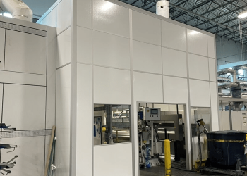 A large modular machine enclosure in a warehouse, designed to isolate machinery and reduce noise and emissions.