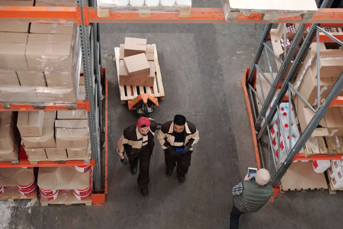 Warehouse workers navigating through organized shelving units with clear pathways and neatly stacked boxes.
