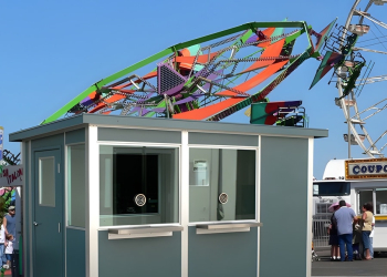 A modular ticketing booth at a carnival, with rides visible in the background.