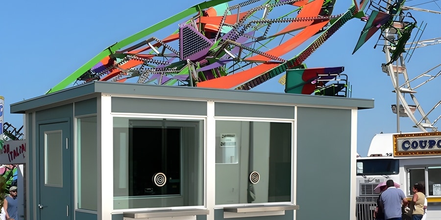 A modular ticketing booth at a carnival, with rides visible in the background.