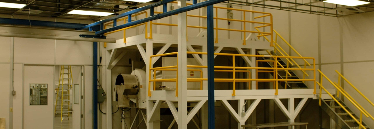 Industrial mezzanine structure with yellow guardrails and stair access, built for additional workspace or equipment storage in a manufacturing or industrial setting.