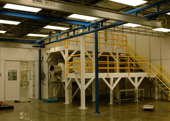 Industrial mezzanine structure with yellow guardrails and stair access, built for additional workspace or equipment storage in a manufacturing or industrial setting.