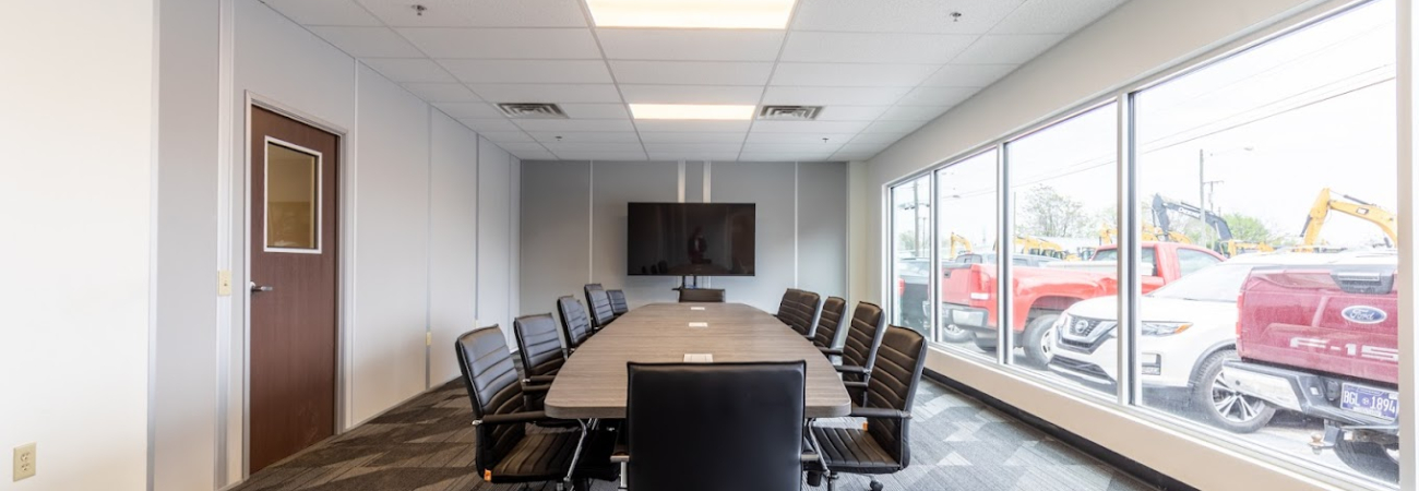 Spacious conference room with modern furnishings inside a modular office building, featuring large windows and a wall-mounted TV.