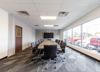 Spacious conference room with modern furnishings inside a modular office building, featuring large windows and a wall-mounted TV.