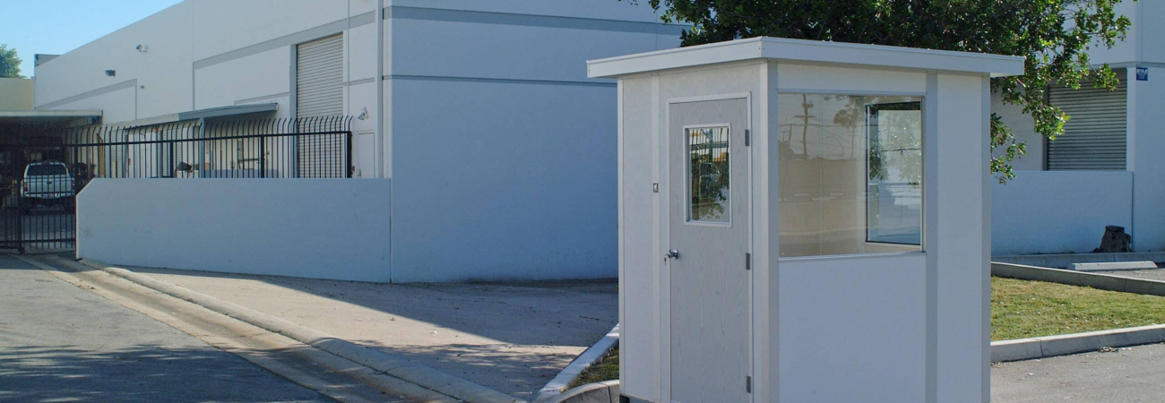 A small white warm-up booth located outdoors near an industrial building, featuring windows and a door.
