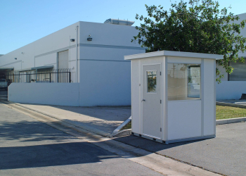 A small white warm-up booth located outdoors near an industrial building, featuring windows and a door.