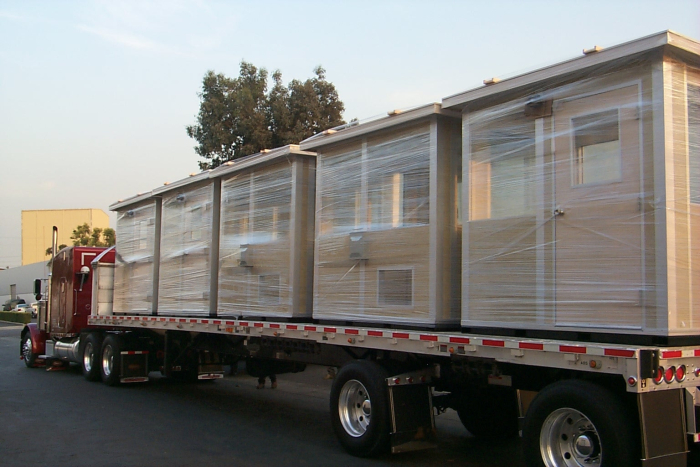 Multiple prefabricated portable guardhouses securely wrapped and loaded on a flatbed truck, ready for delivery.