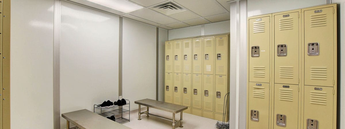 Modular locker room with stainless steel benches, beige lockers, and ceiling ventilation for controlled environments.