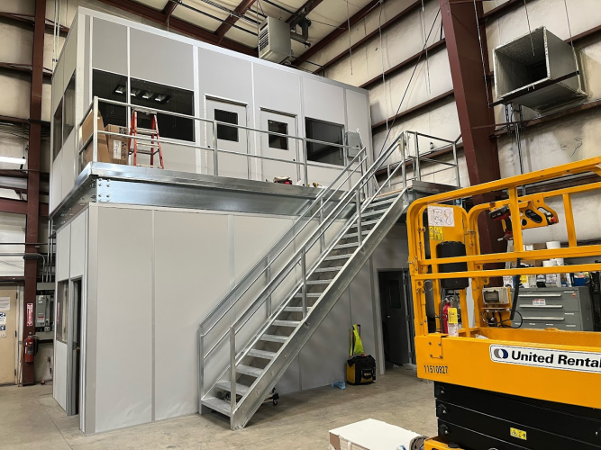 Elevated mezzanine structure with a modular office and metal staircase inside an industrial warehouse.