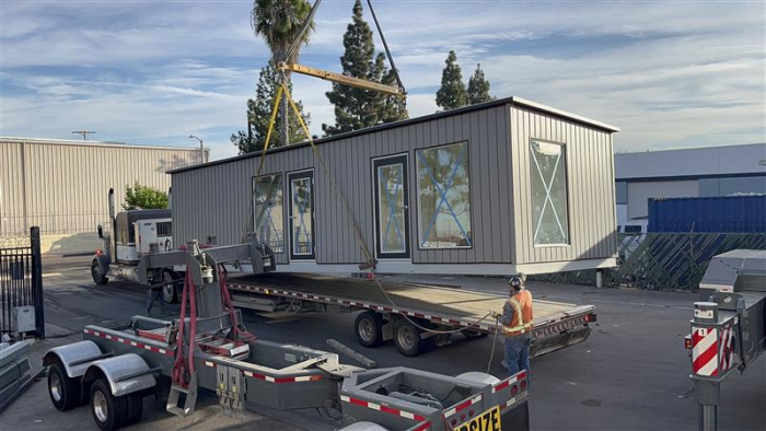 Portable modular office being loaded onto a flatbed truck for transport, showcasing its prefabricated design and large windows.