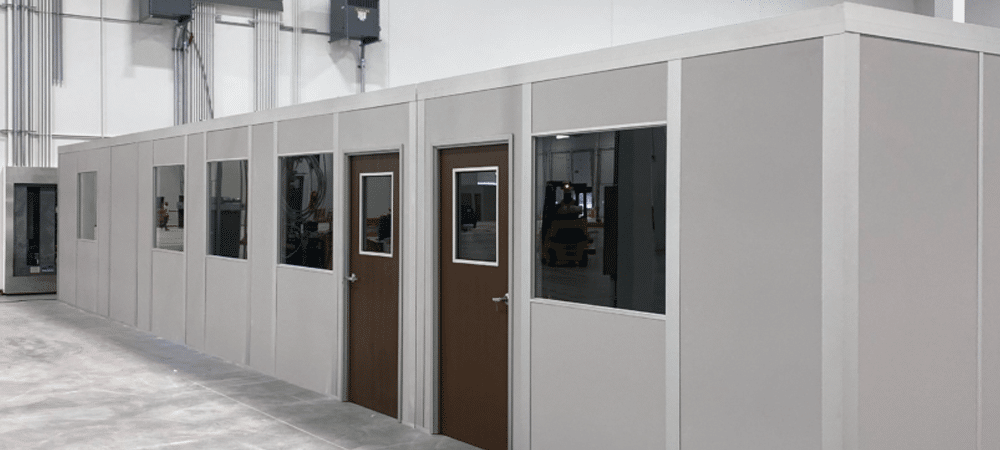 Modular inplant office installed in an industrial warehouse, featuring multiple doors, windows, and a clean, prefabricated design.