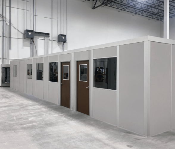 Modular inplant office installed in an industrial warehouse, featuring multiple doors, windows, and a clean, prefabricated design.