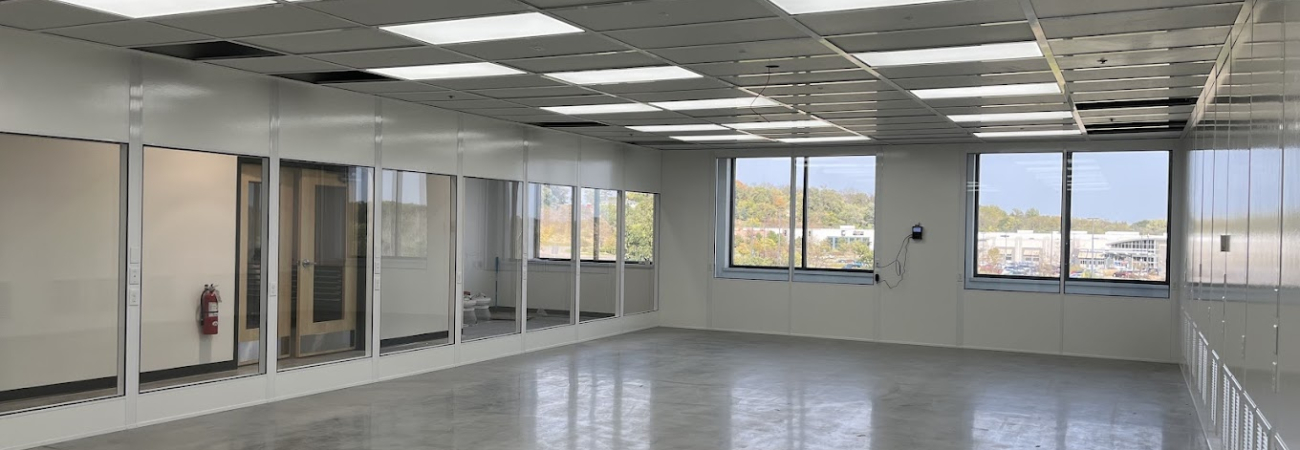 Spacious modular office interior with large windows, glass-paneled walls, and bright overhead lighting, showcasing a modern and versatile workspace design.