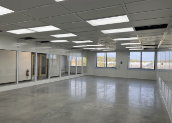 Spacious modular office interior with large windows, glass-paneled walls, and bright overhead lighting, showcasing a modern and versatile workspace design.