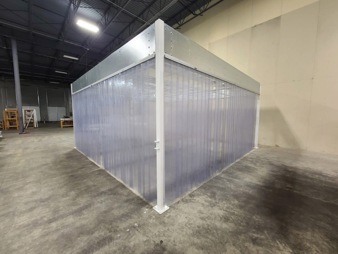 Portable softwall cleanroom with clear panels and a sturdy metal frame, set up inside a warehouse for controlled operations.