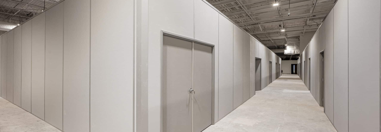A large inplant modular office inside an industrial facility, featuring clean, gray panel walls, a double-door entrance, and a spacious hallway with multiple office units under an exposed ceiling structure.