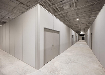 A large inplant modular office inside an industrial facility, featuring clean, gray panel walls, a double-door entrance, and a spacious hallway with multiple office units under an exposed ceiling structure.