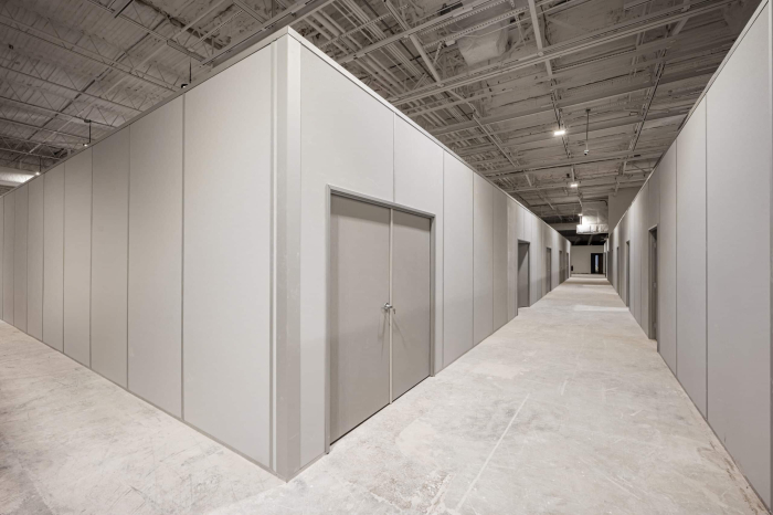A large inplant modular office inside an industrial facility, featuring clean, gray panel walls, a double-door entrance, and a spacious hallway with multiple office units under an exposed ceiling structure.