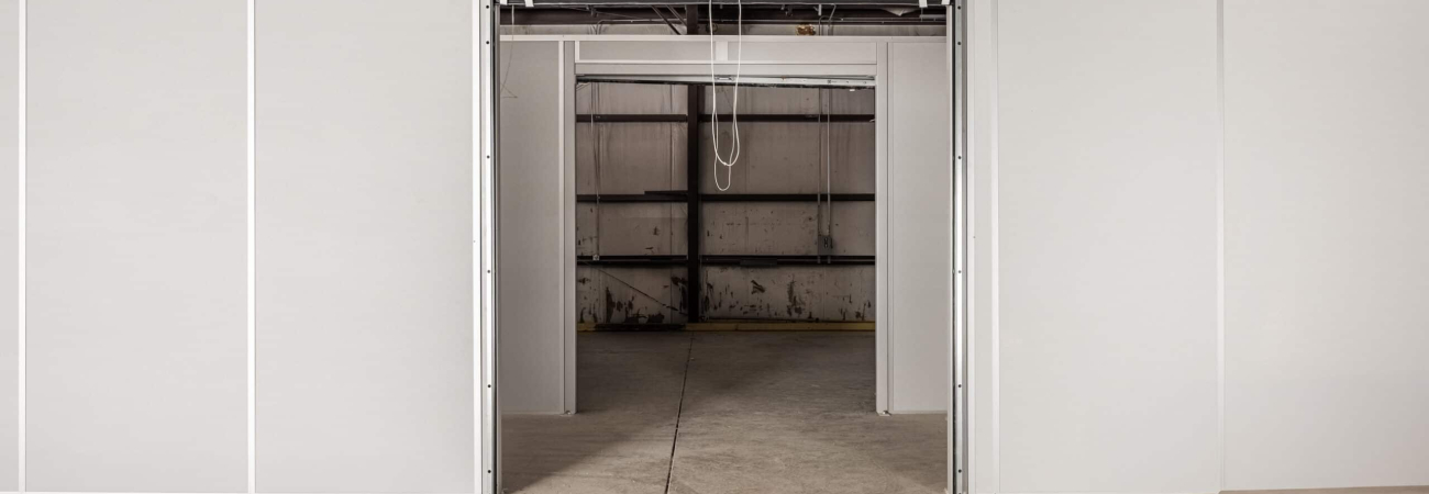 Modular warehouse partition with a roll-up door, dividing a large open space into smaller, customizable sections.