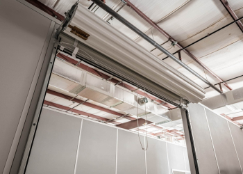 An interior shot of an Allied Modular modular enclosure featuring clean, prefabricated wall panels, steel support beams, and an overhead roll-up door. The factory-built, reusable wall systems shown here are the type of modular construction that can earn up to 25 points toward LEED certification.
