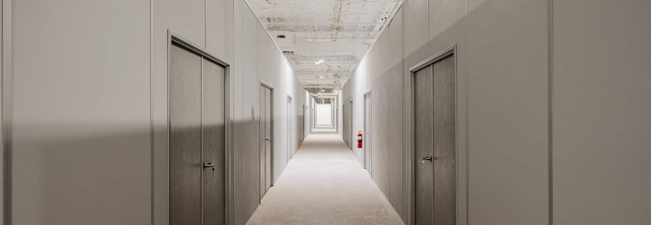 A long hallway in a warehouse featuring modular wall dividers with doors, creating separate rooms for storage or office use.