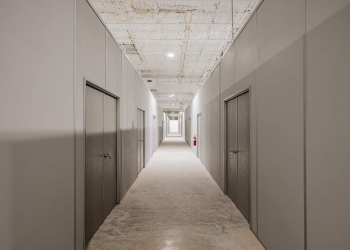 A long hallway in a warehouse featuring modular wall dividers with doors, creating separate rooms for storage or office use.
