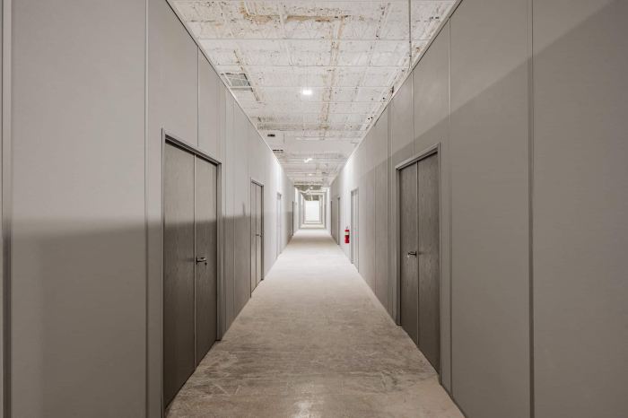 A long hallway in a warehouse featuring modular wall dividers with doors, creating separate rooms for storage or office use.